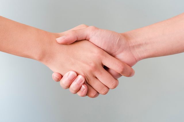Zwei Hände geben sich die Hand vor hellgrauem Hintergrund