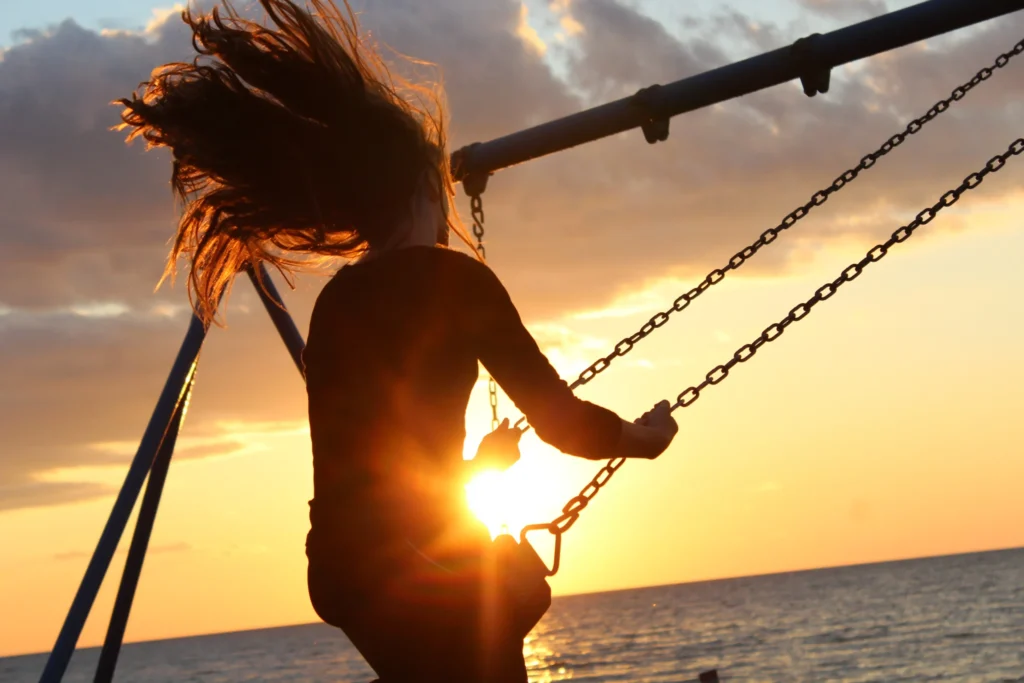 die glueckshexe: Eine Frau schaukelt in den Sonnenuntergang über dem Meer